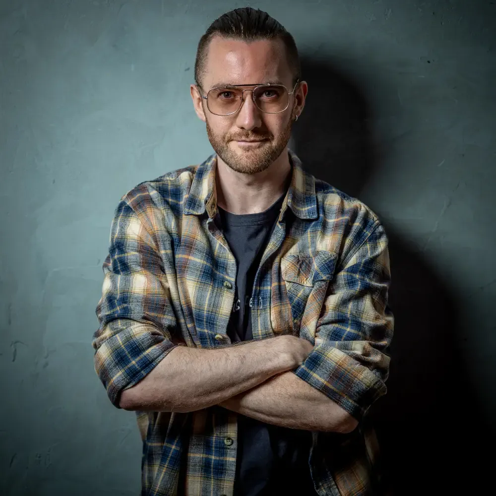 Porträt von Michael Wolf mit Brille und kariertem Hemd, die Arme verschränkt, vor einer blaugrauen Wand
